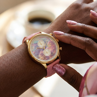 Pink unicorn watch with a gold case, iridescent dial, and pink leather strap worn on a wrist with glittery nails.