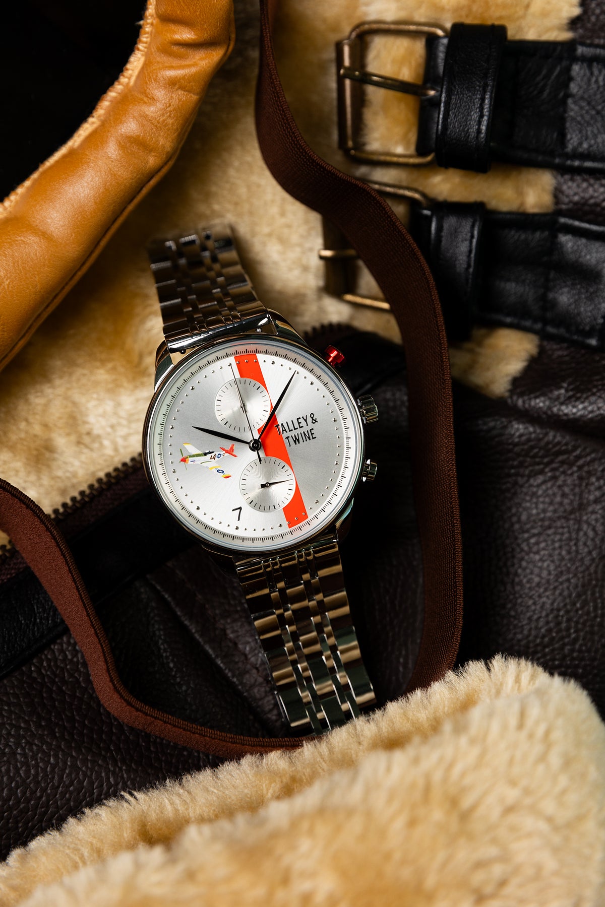Tuskegee Airmen Red Tails watch with silver band, white dial, red accents, placed on a brown leather jacket.
