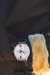 Tuskegee Airmen Red Tails watch with a silver dial, red accents, and a stainless steel bracelet worn on a wrist.