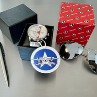 Tuskegee Airmen Red Tails watch displayed with a black box, sunglasses, and a silver pen on a gray surface.